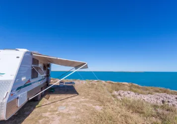 RV awning extended on travel trailer in front of water view