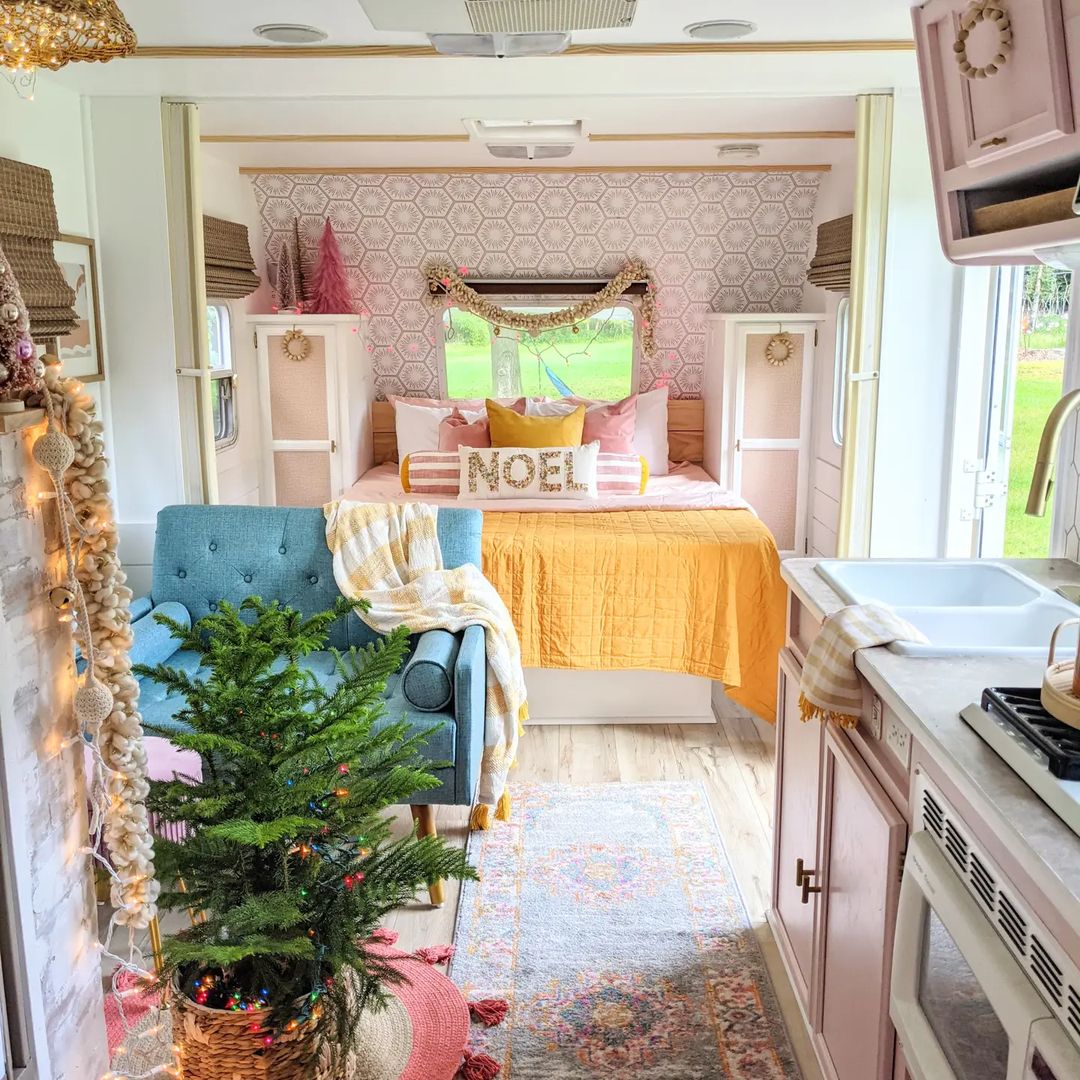 RV interior shot featuring pink wallpaper, soft blue couch, and pink cupboards.