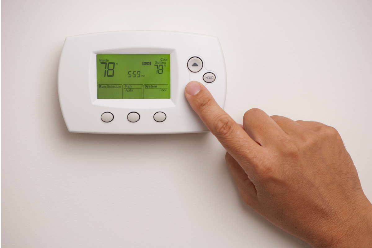 Close up of a hand adjusting the temperatire on a wall mounted digital thermostat - RC AC unit