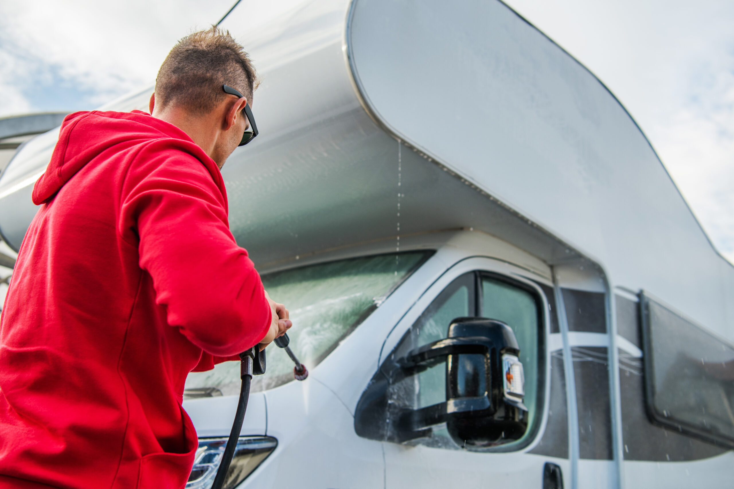 man washing an RV with a pressure washer - feature image for How To Dewinterize An RV