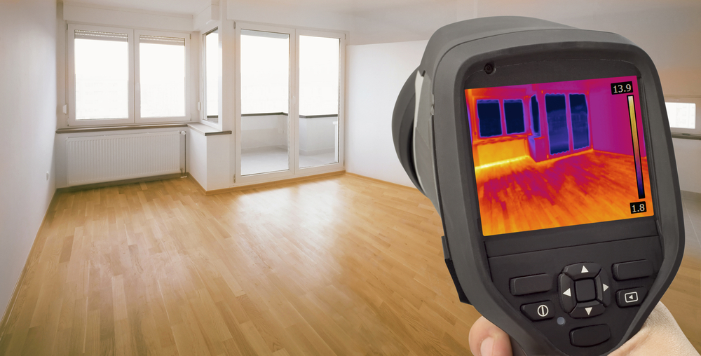 Hand holding a thermal camera viewing an empty room for heat loss.