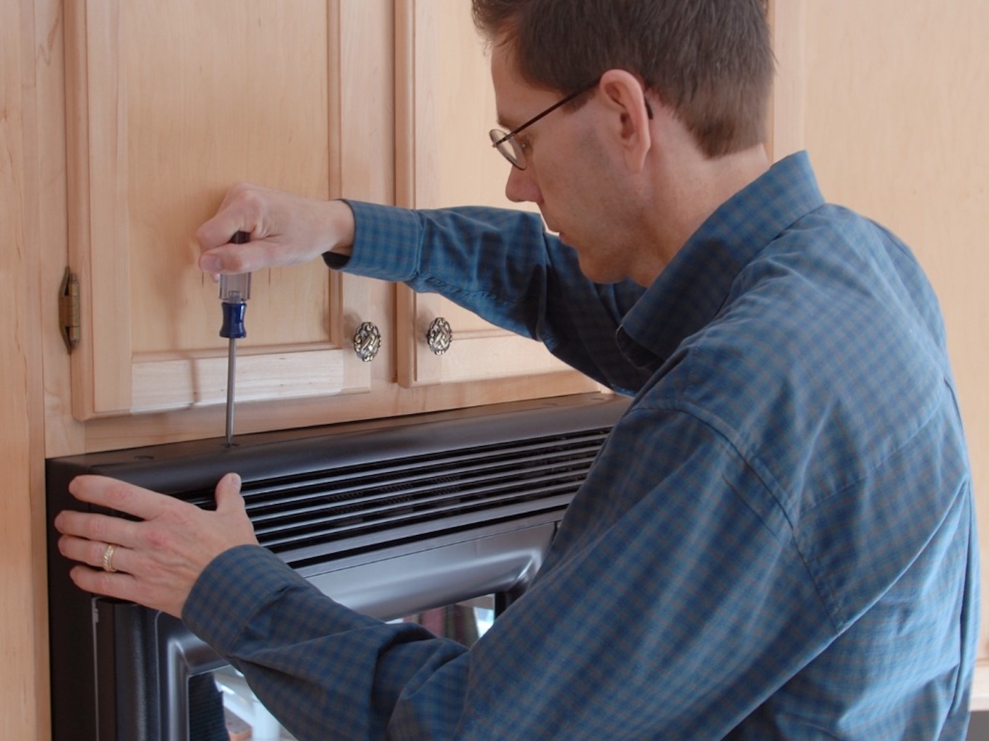 A man wearing glasses with a screwdriver tries RV microwave replacement 
