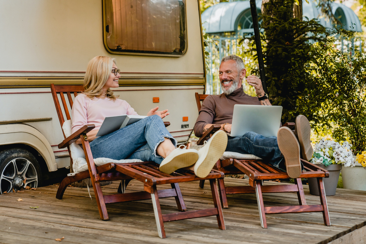 bearded caucasian man and woman seated and relaxing in front of RV with open laptop using internet -  feature image for RV park internet solutions