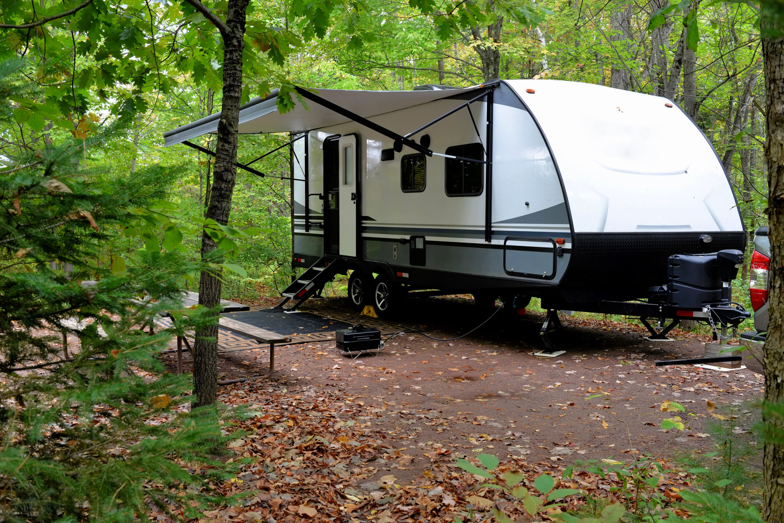 Travel trailer sits at a campsite in the woods.