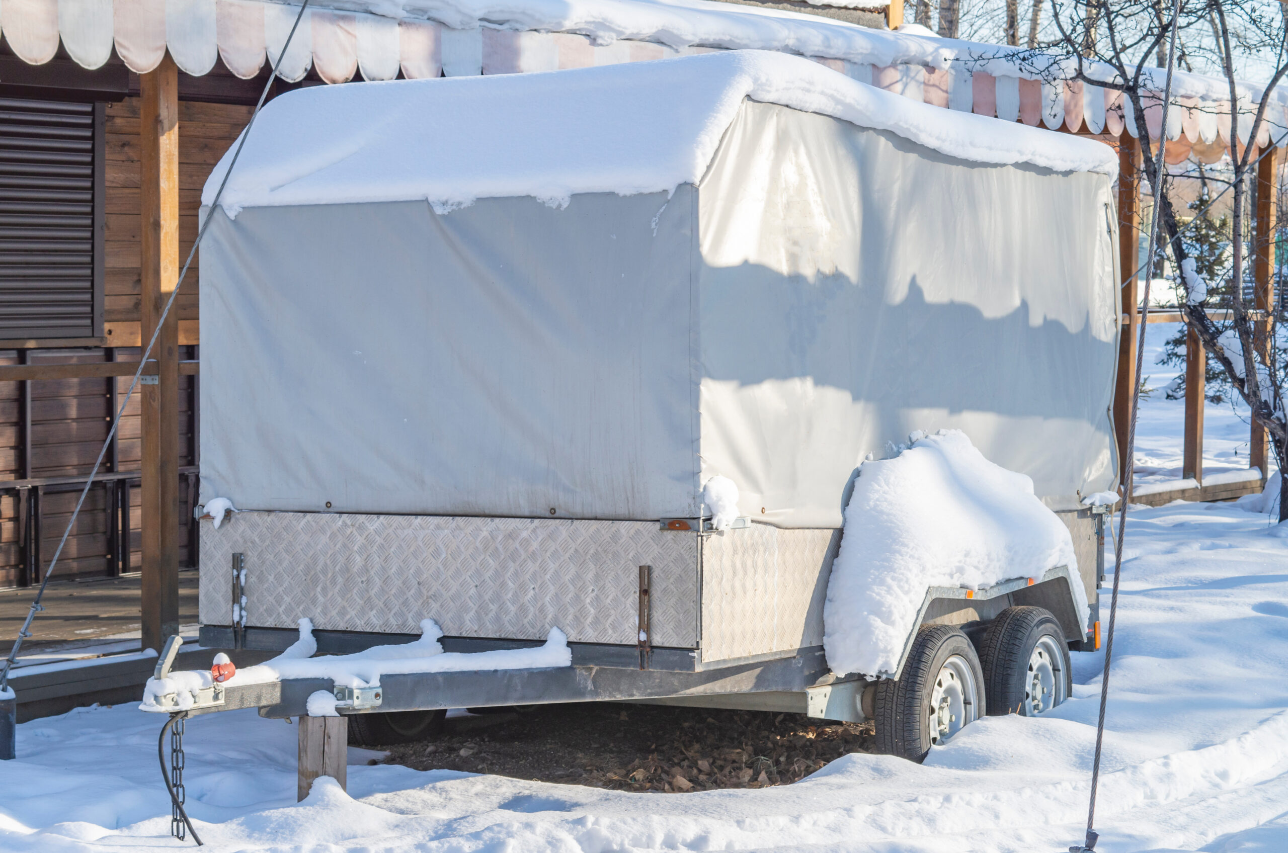 trailer with cover in snow - feature image for how to winterize an RV