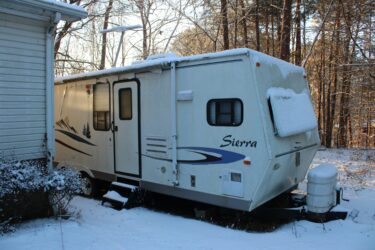 trailer in snow outside of house - feature image for how to winterize an RV
