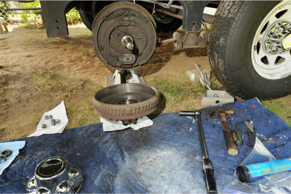 Trailer tire removed exposing disassemblyed brakes with tools laid out on a mat - preventative maintenance