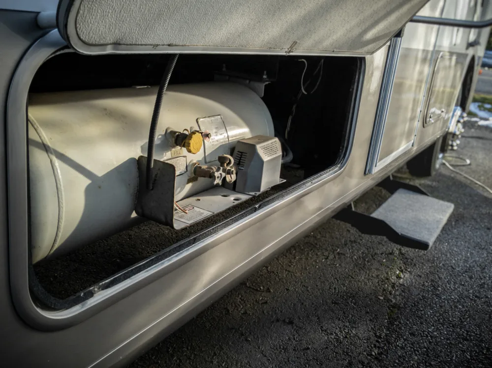 An RV propane tank mounted in a motorhome. The valve is open to allow operation of the RV fridge while driving.