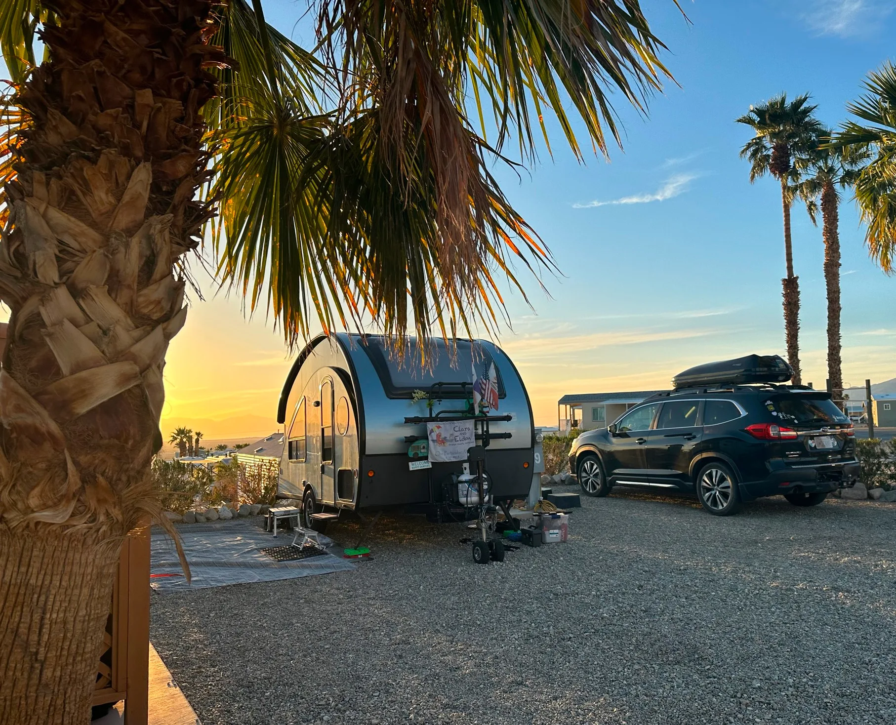 a couple of cars parked in a parking lot next to a palm tree and a camper on the side of the road