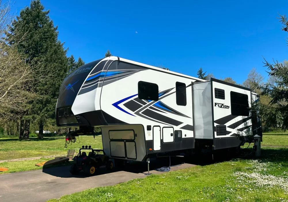 a white and blue rv parked on the side of a road next to a field of grass and trees