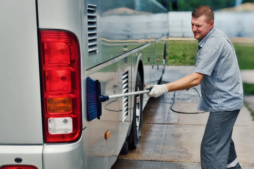 A man washes his rv on the road using a soft brush.