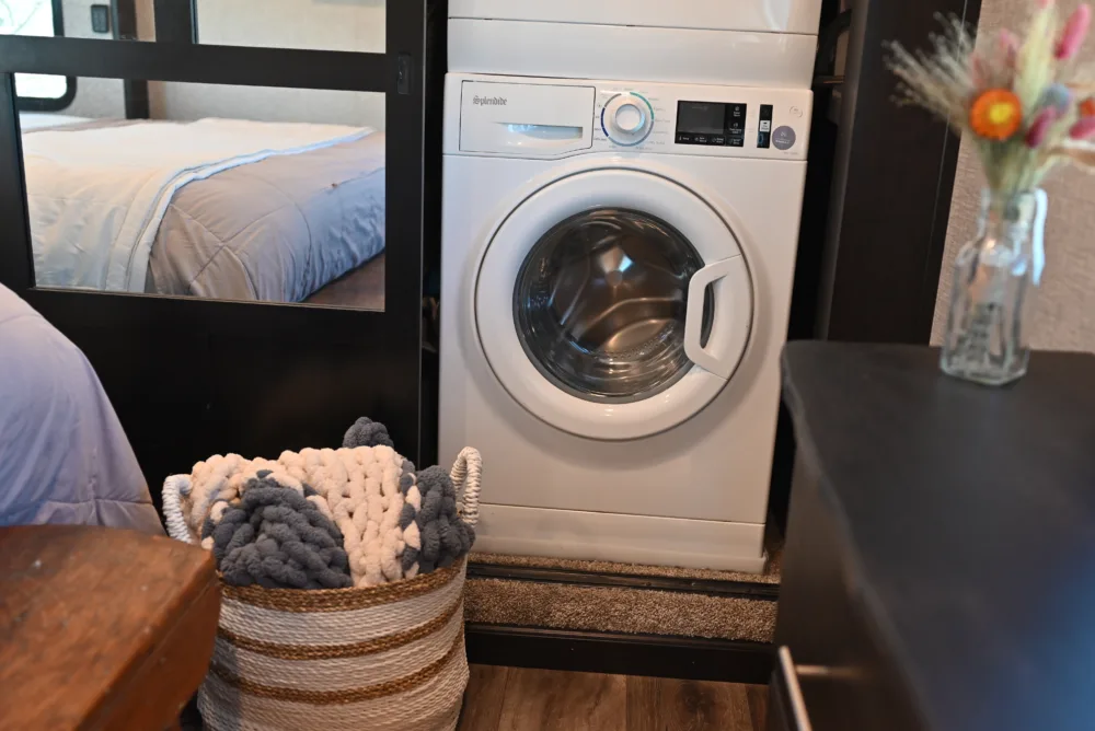 a white washer sitting next to a bed with a vase of flowers on the side of the washer