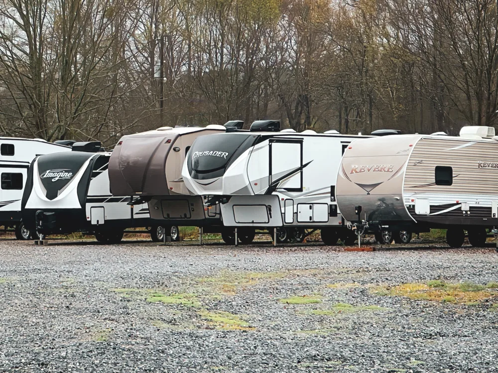 a row of rvs parked next to each other on a gravel road in front of a wooded area, storage, image for winterizing