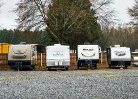 a row of travel trailers parked next to each other in front of a wooden fence with trees in the background, RV storage, image for winterizing