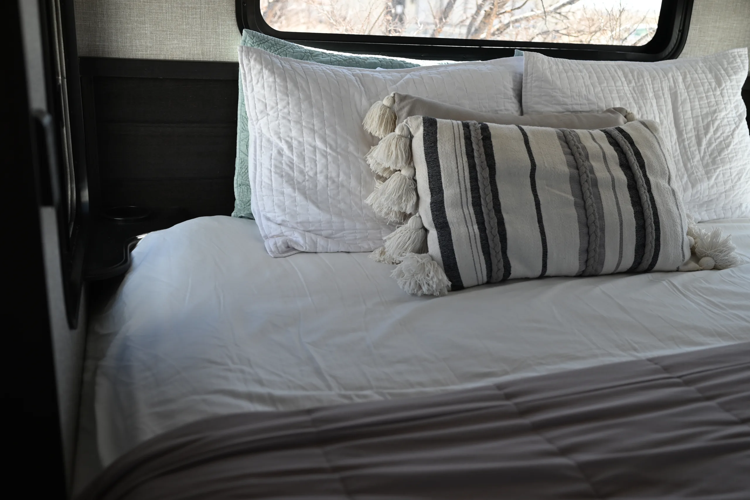 a white bed with a black and white pillow and a black and white striped pillow on top of it, image for RV heated mattress pads
