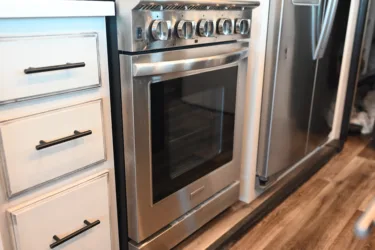 a silver stove top oven sitting inside of a kitchen next to a white counter top and a wooden floor