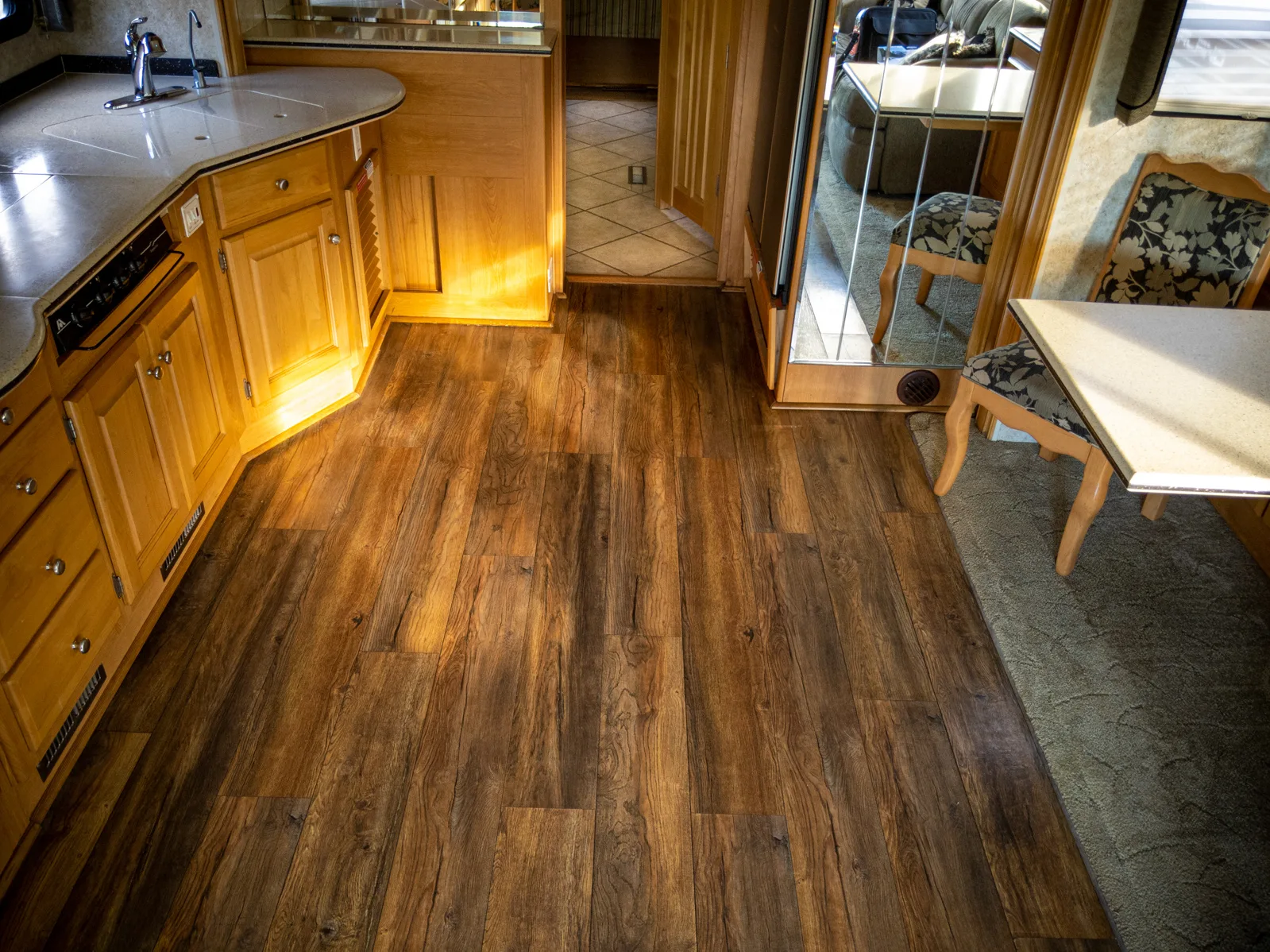 a wooden floor in a kitchen next to a dining room table and a kitchen with a stove top oven, image for vinyl flooring RV
