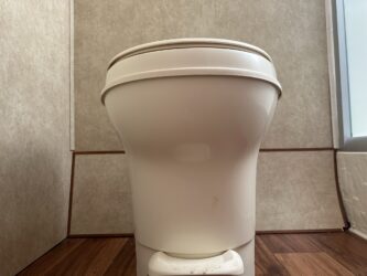 a white toilet sitting in a bathroom next to a toilet paper dispenser on a wooden floor, image for R