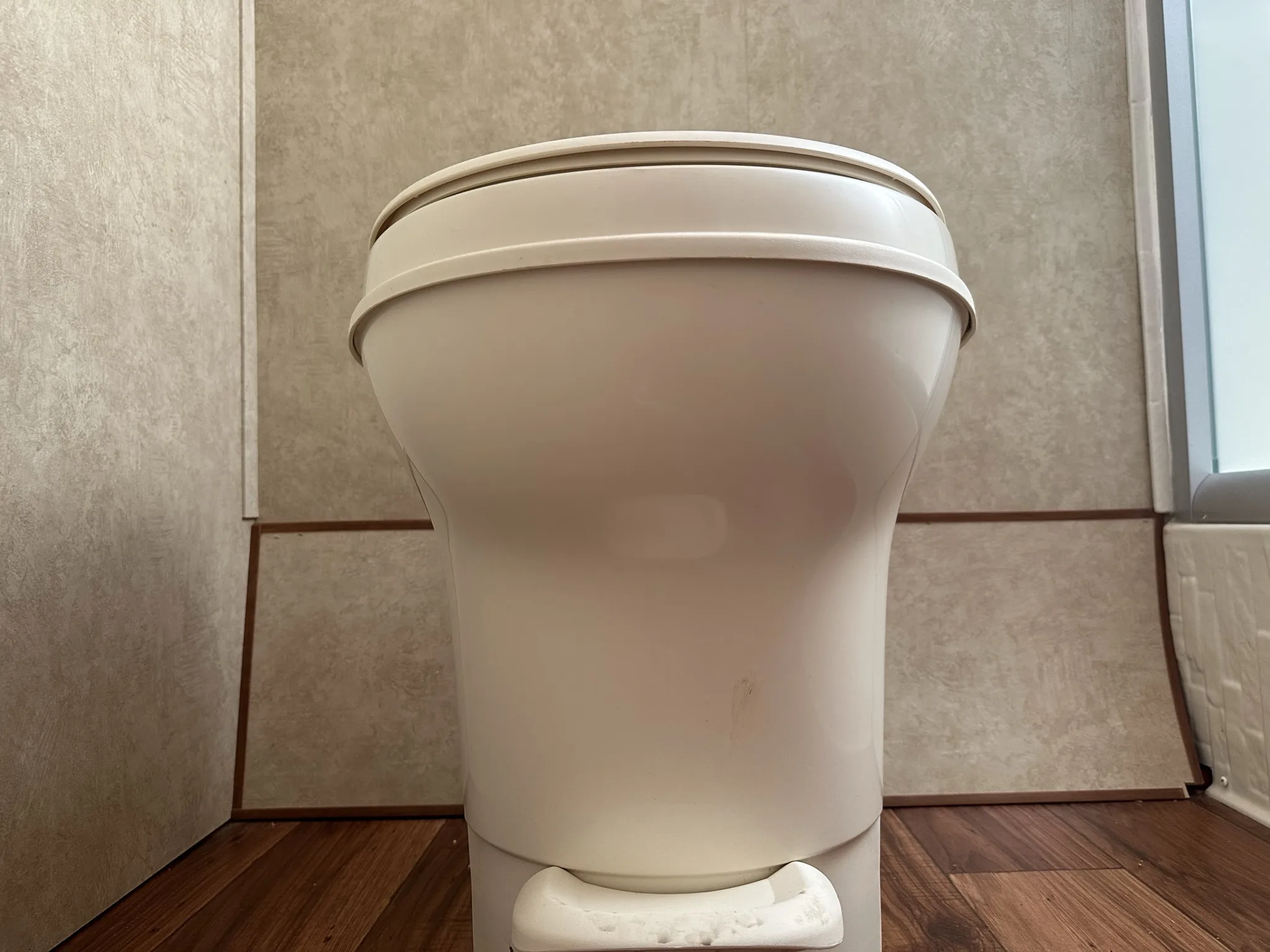 a white toilet sitting in a bathroom next to a toilet paper dispenser on a wooden floor, image for R