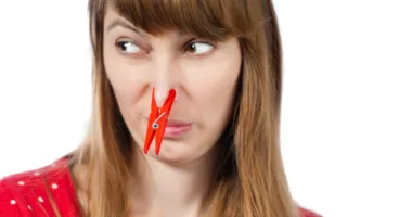 young woman with red clothespin on her nose trying to not get a whiff of bad smells