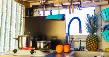 RV kitchen area with pans on stovetop, sink, and utensils hanging from a magnet strip