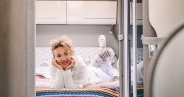 Cheerful serene young adult woman laying in the bedroom inside a modern camper van motor home.