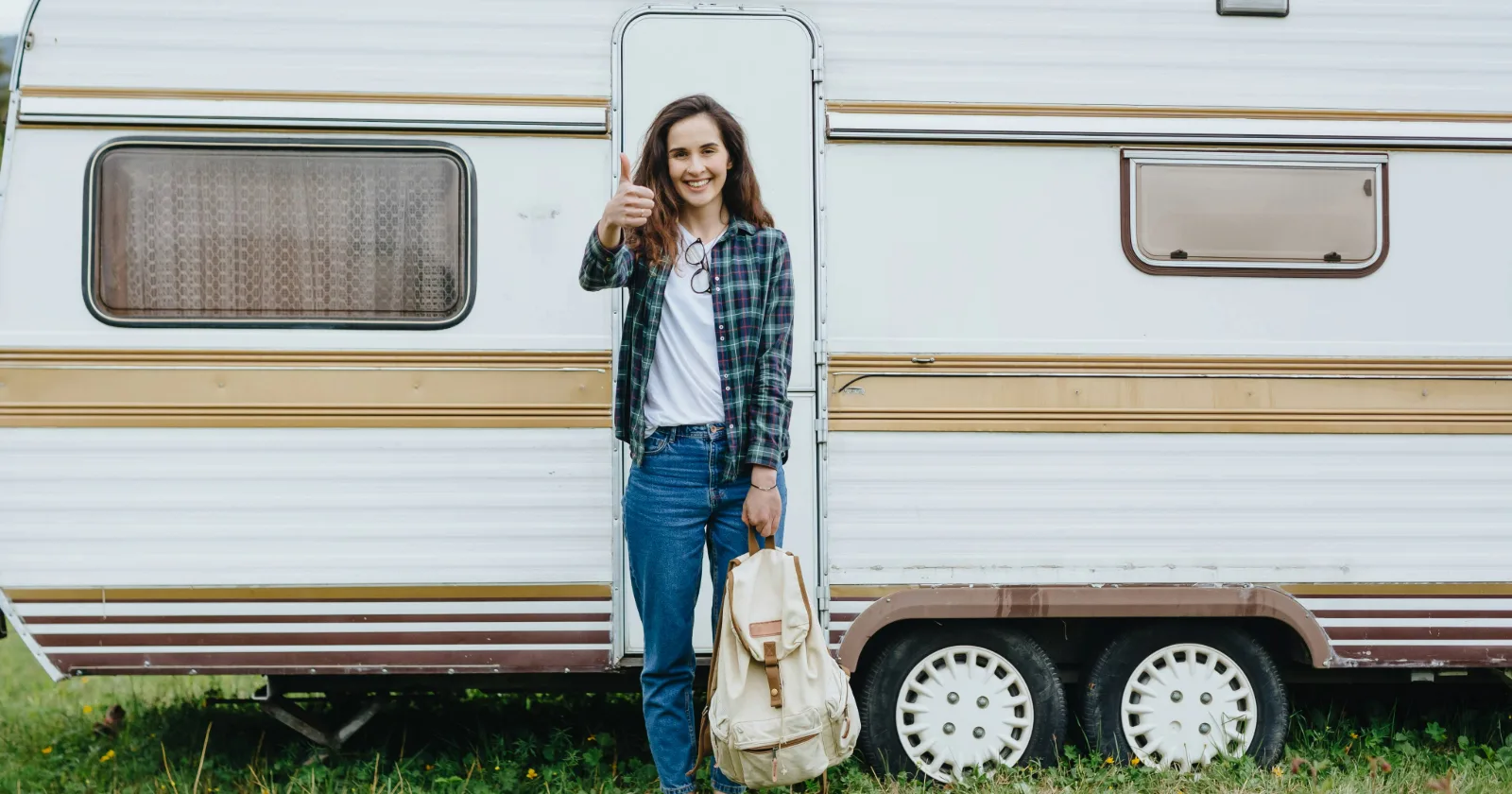 Girl standing in front of travel trailer giving the thumbs up