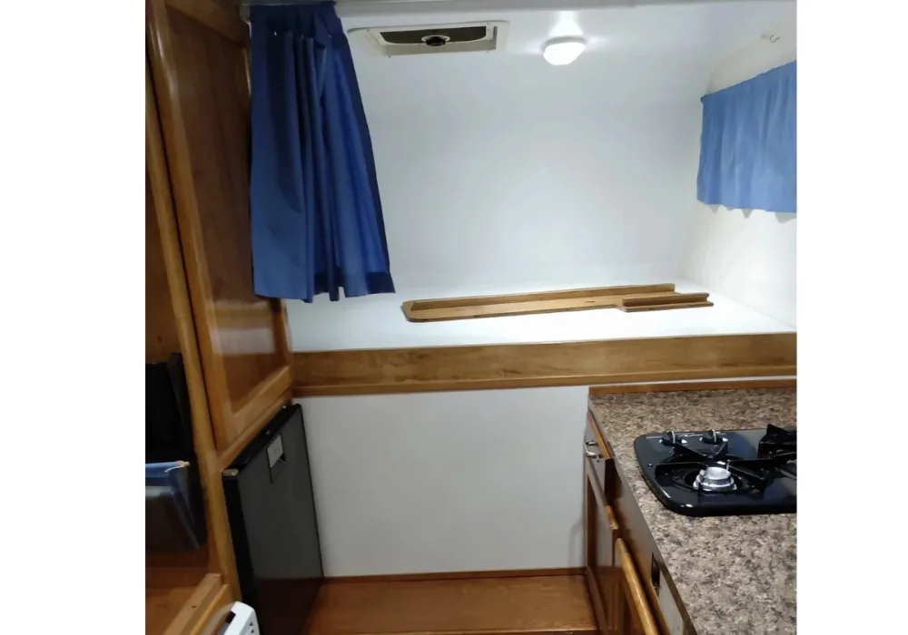 interior of camper with bed platform, cabinets, refrigerator, and burner