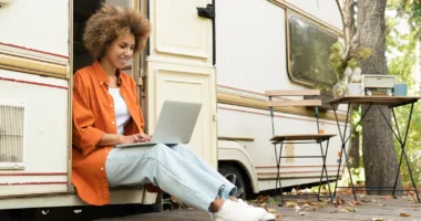 Young woman at work with her RVing job, typing on laptop while sitting in doorway of RV
