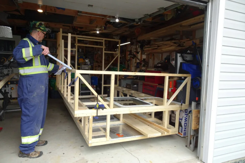 Man working on the frame of a green teardrop camper build in a garage