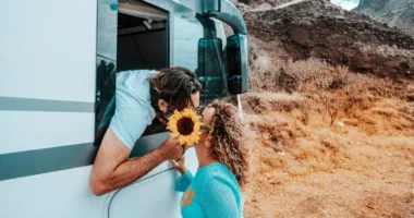 Man reaching down from RV window to woman for a kiss. Flower is blocking their faces.