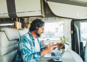 man in the middle of a Zoom call with headphones on, talking to laptop screen, and sitting at the dining table of his RV using time management skills productively