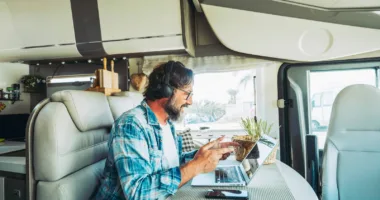 man in the middle of a Zoom call with headphones on, talking to laptop screen, and sitting at the dining table of his RV using time management skills productively