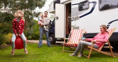 family lounging and playing outside of motorhome at campsite as RV weekend warriors
